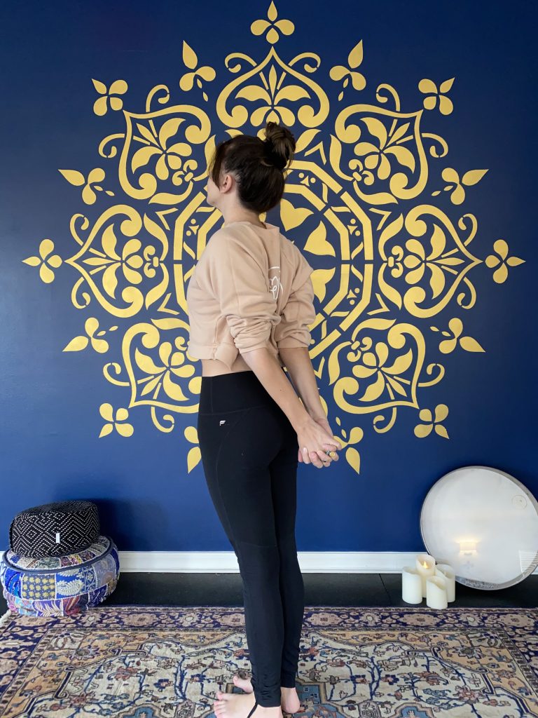 Image of yoga teacher with hands clasped behind her low back