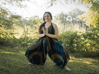 A student standing in a wide-legged pose with hands at heart centre, outdoors in evening light.
